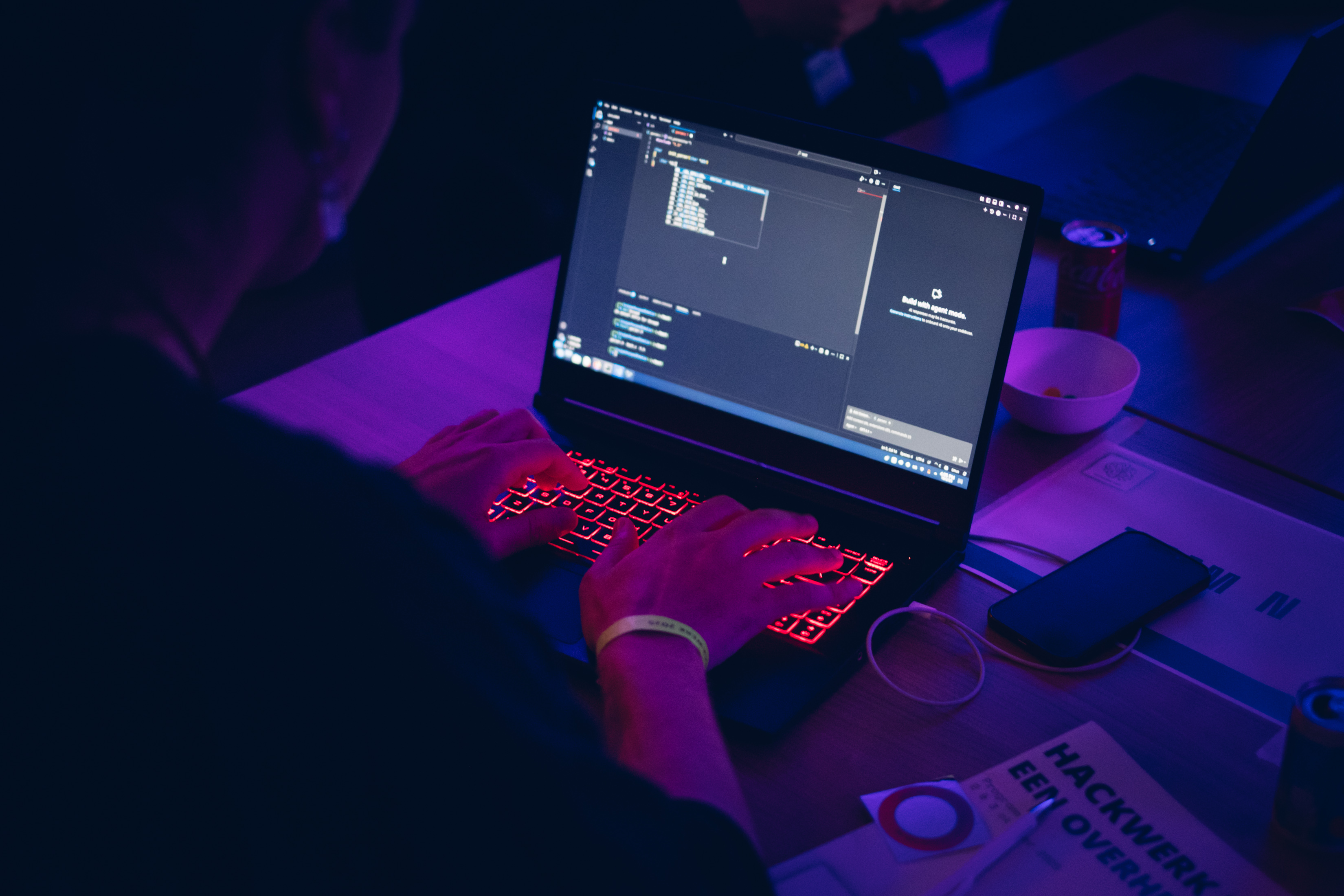 Deelnemers coderen tijdens Hackwerk2025 met hun code op groot scherm